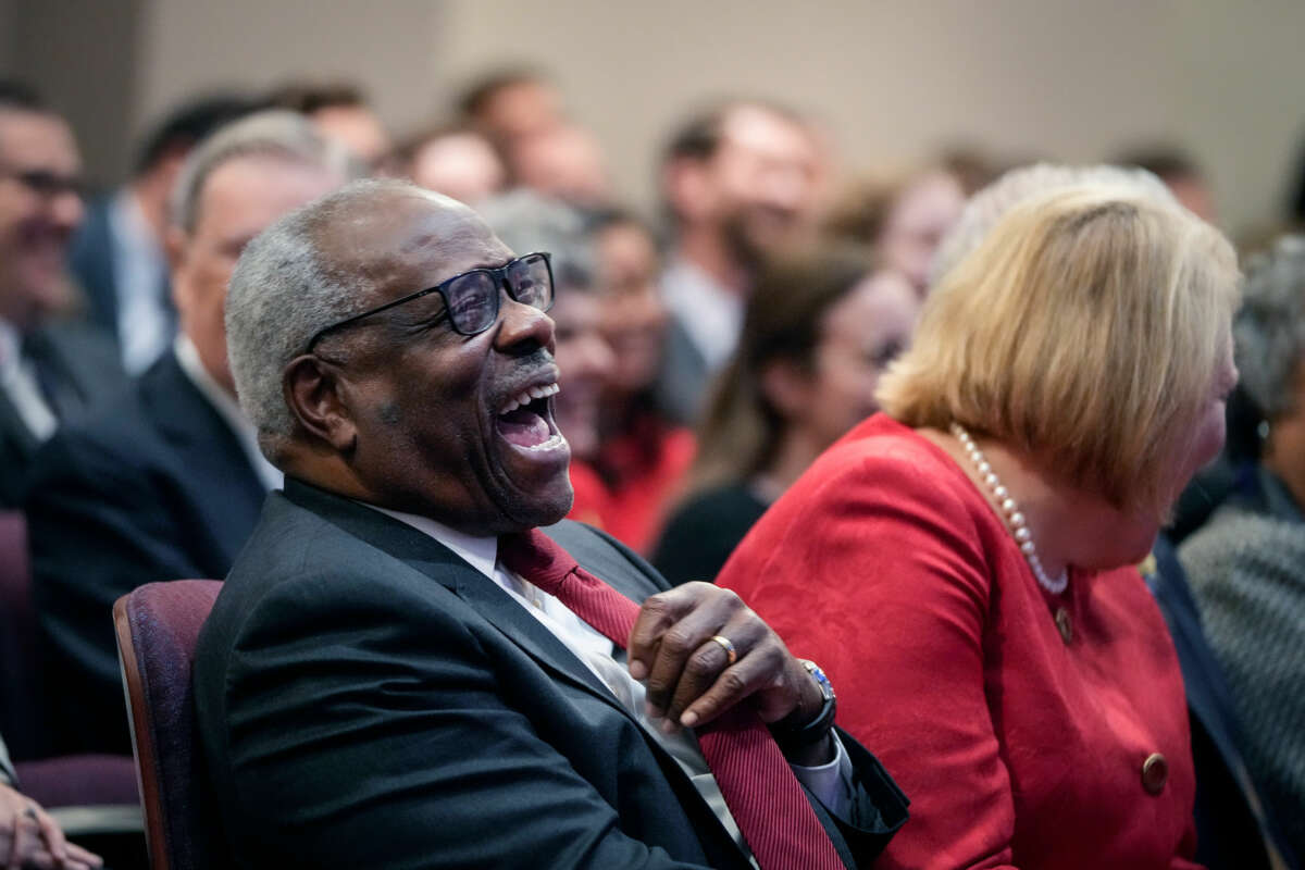 Justice Clarence Thomas laughs uproariously at something while seated next to his wife