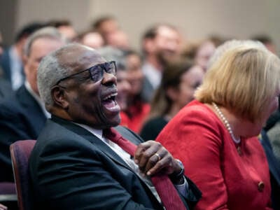Justice Clarence Thomas laughs uproariously at something while seated next to his wife