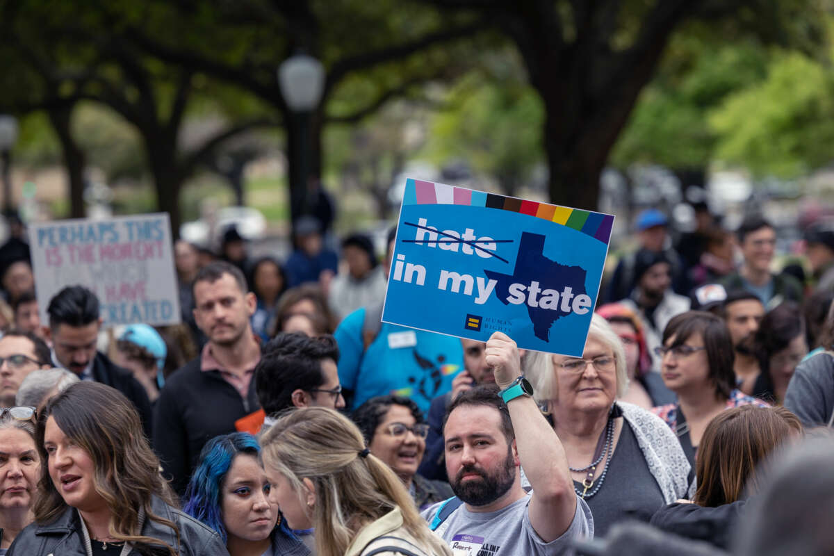 A protester holds up a sign reading "NO HATE IN MY STATE" while participating in an outdoor protest