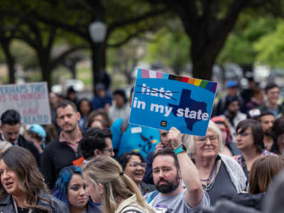 A protester holds up a sign reading "NO HATE IN MY STATE" while participating in an outdoor protest