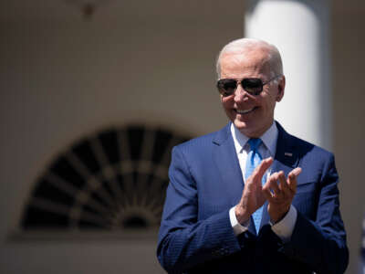 Joe Biden claps while wearing aviator sunglasses.