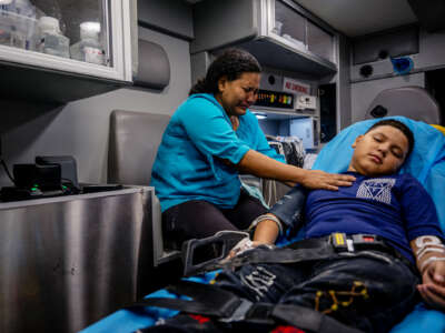 A mother cries beside her unconscious child in the back of an ambulance