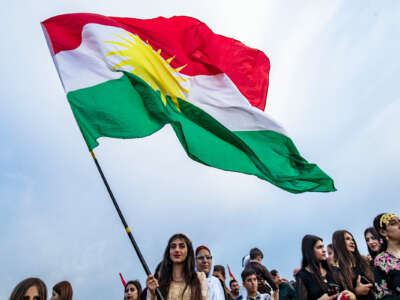 Kurdish women hold aloft the flag of Kurdistan while celebrating outdoors