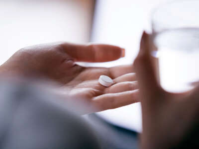 Close up woman holding pill in hand with water.