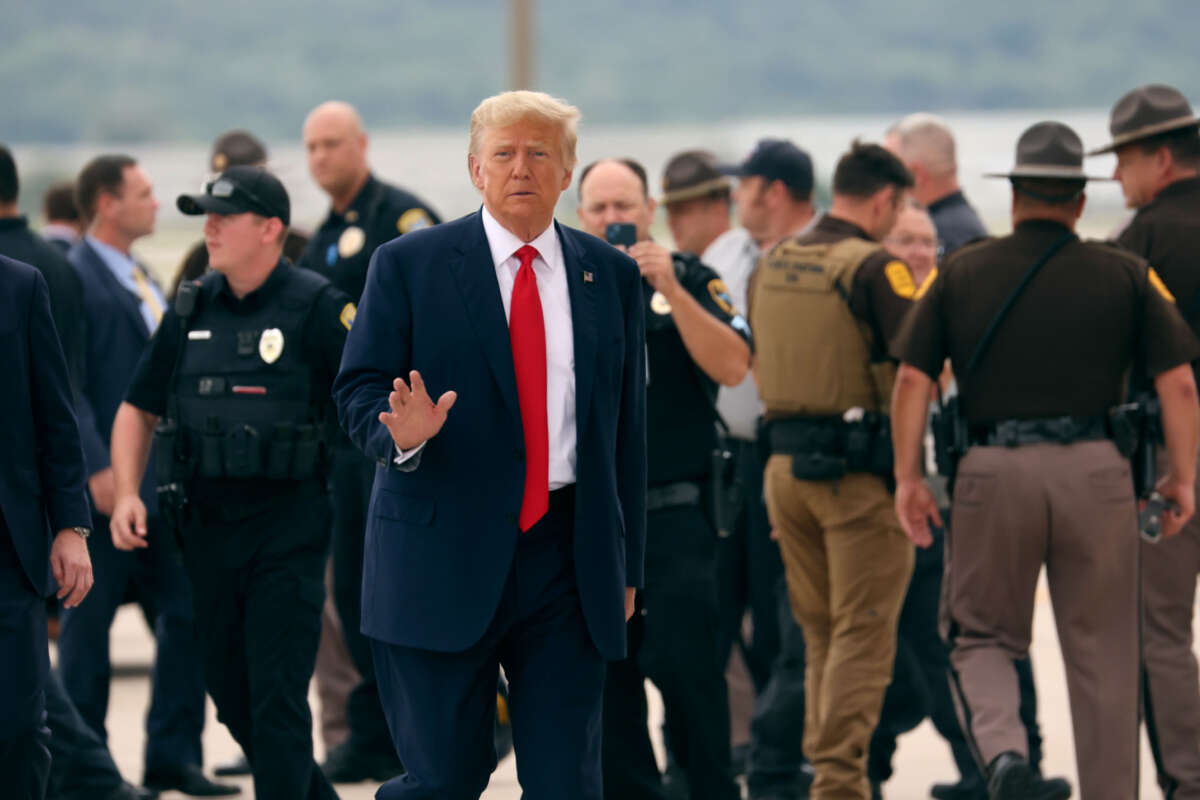 Former President Donald Trump waves as he walks in front of law enforcement officers outside at an airport.