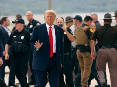 Former President Donald Trump waves as he walks in front of law enforcement officers outside at an airport.