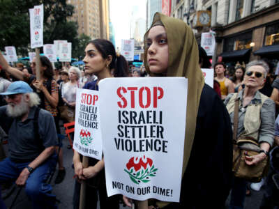 A protester holds a sign reading "STOP ISRAELI SETTLER VIOLENCE; NOT ON OUR DIME" during an outdoor demonstration