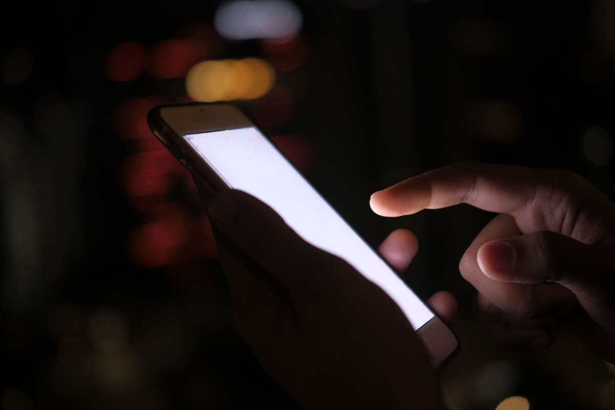 Person using lit-up cell phone in dark area