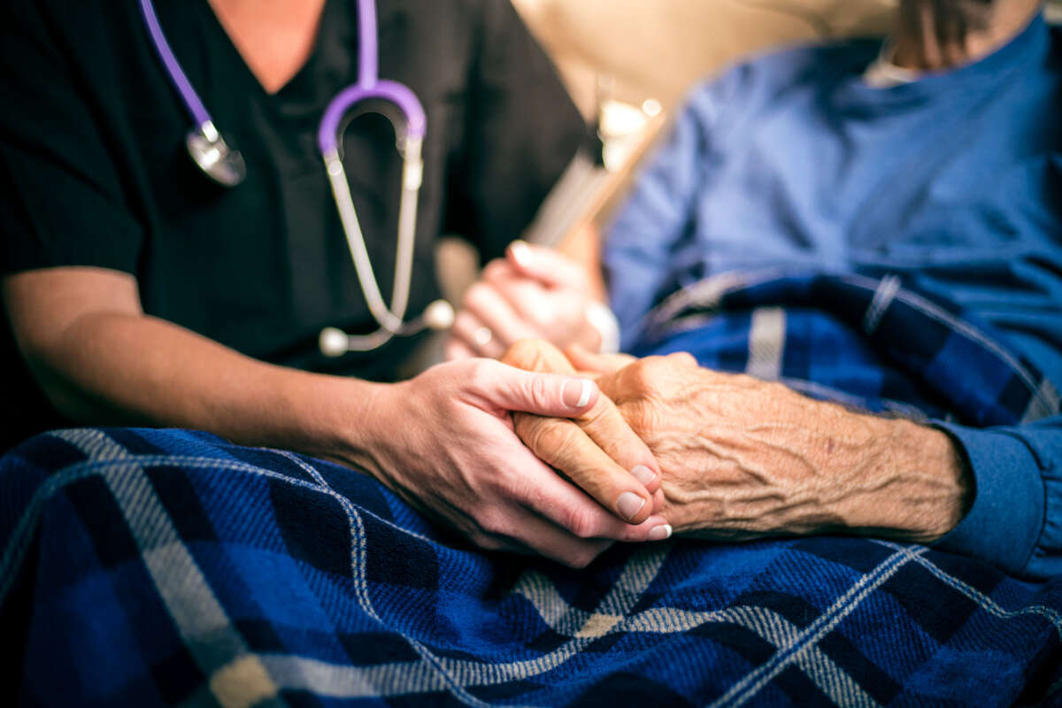 Hospice nurse holds the hands of an elderly patient