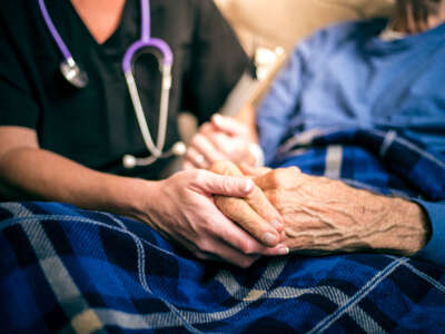 Hospice nurse holds the hands of an elderly patient