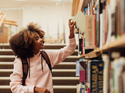 Young student takes book from library shelf