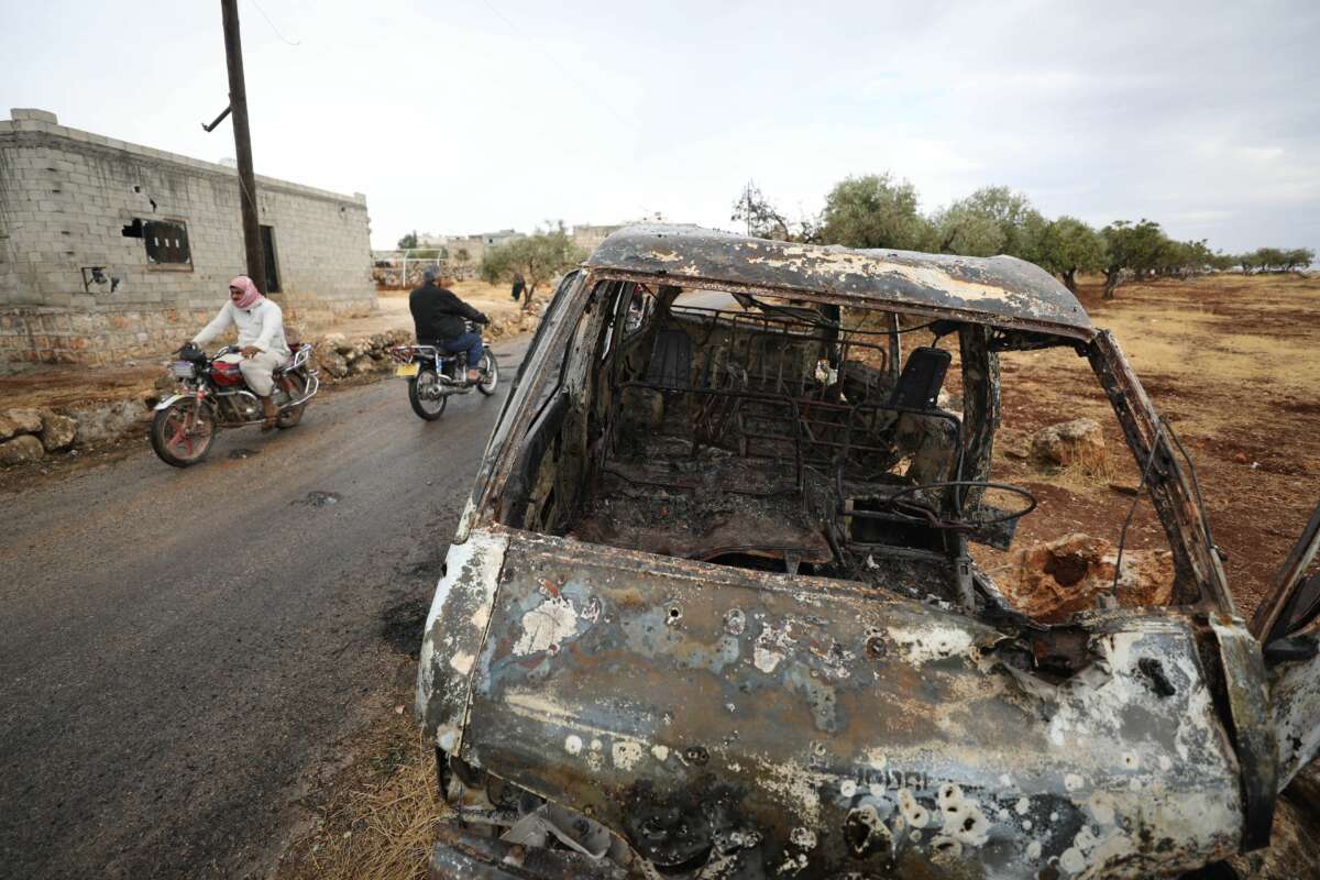 Bikers ride past a damaged car at the site of a suspected US-led operation against Islamic State chief Abu Bakr al-Baghdadi the previous day, on the edge of the small Syrian village of Barisha in the country's opposition-held northwestern Idlib province, on October 28, 2019.