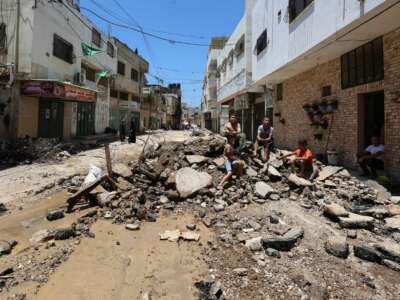 People sit amid the rubble along a street in the occupied West Bank Jenin refugee camp on July 6, 2023, following a large-scale Israeli military raid that lasted for two days.