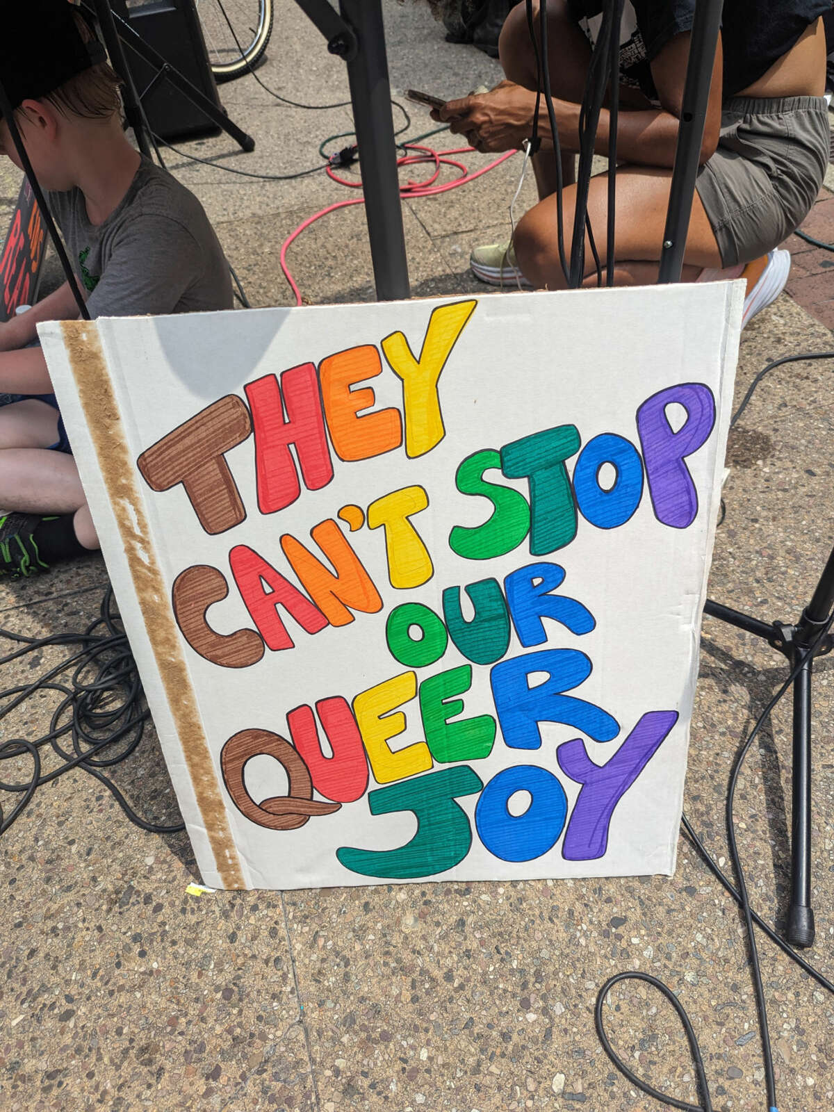 A sign reading "They can't stop our queer joy" rests against the speaker stand on July 2, 2023.