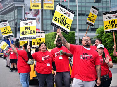 People in red shirts display signs reading "ON STRIKE" and "EN HUELGA" during an outdoor demonstration