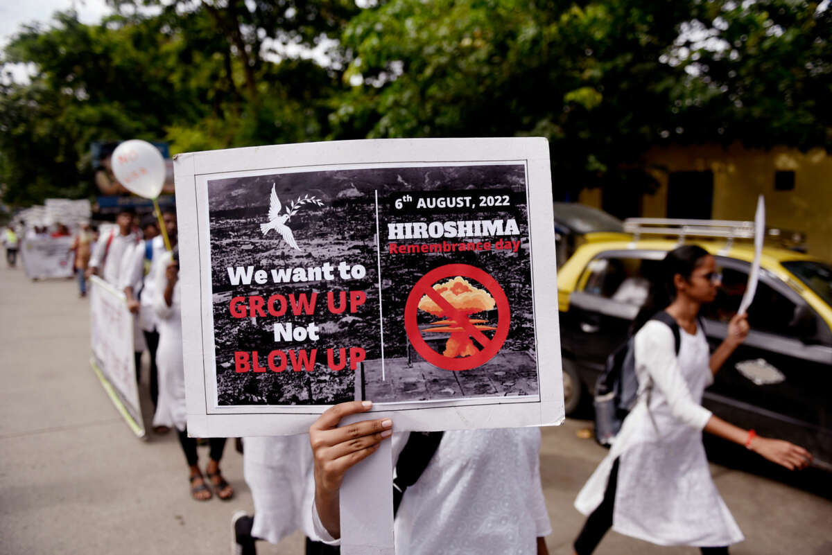 A protester holds a sign reading 'WE WANT TO GROW UP, NOT BLOW UP" alongside a photo of a nuclear warhead explosion