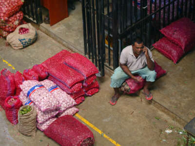 A vendor speaks to someone on the phone while seated next to large bags of produce for sale