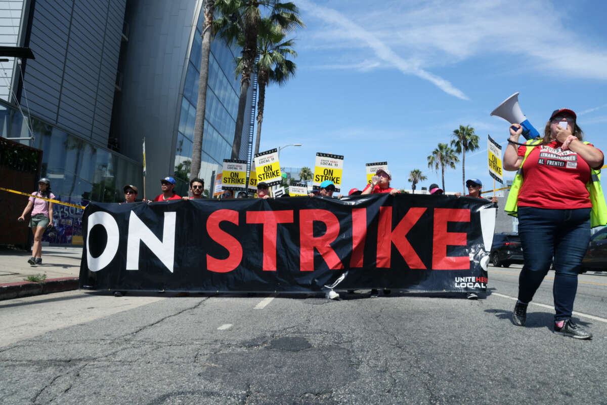 People march behind a banner reading "ON STRIKE" as a person chants on a megaphone