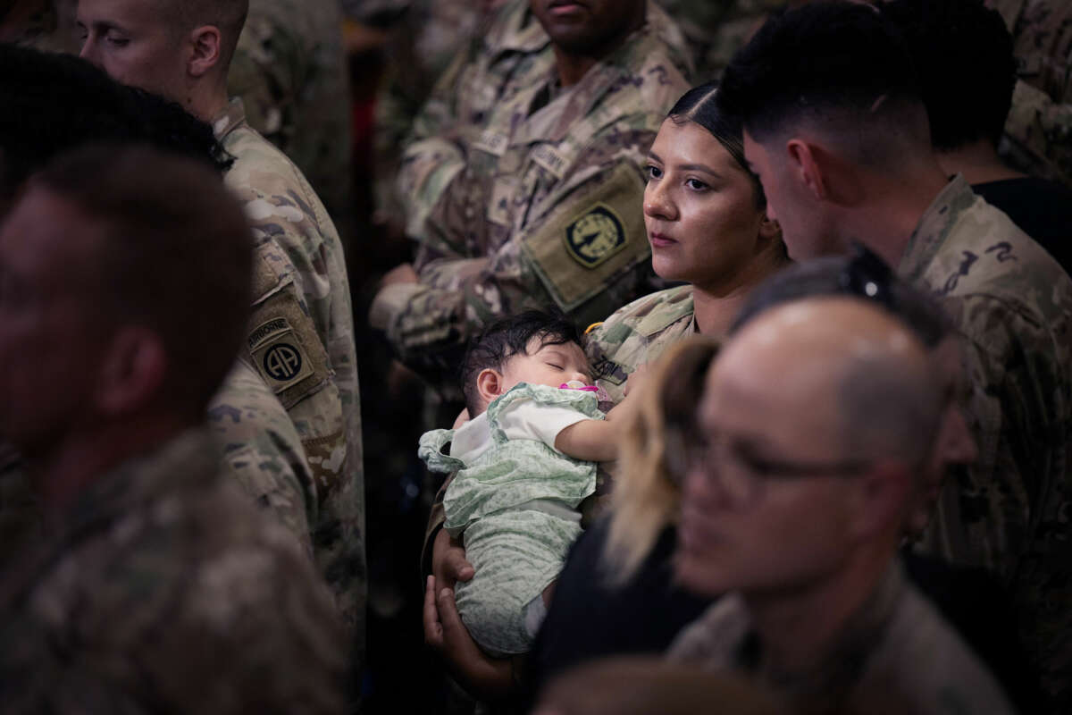 A woman in military uniform holds her infant child as she stands among others, also in uniform