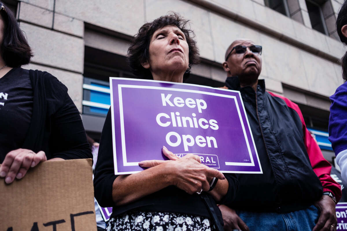 A solemn protester closes her eyes while holding a sign reading "Keep clinics open"