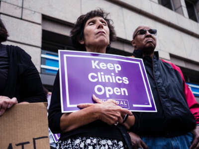 A solemn protester closes her eyes while holding a sign reading "Keep clinics open"