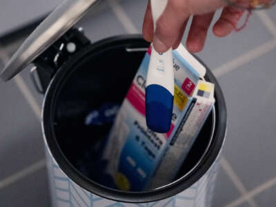 A hand prepares to throw a positive pregnancy test into a trash can