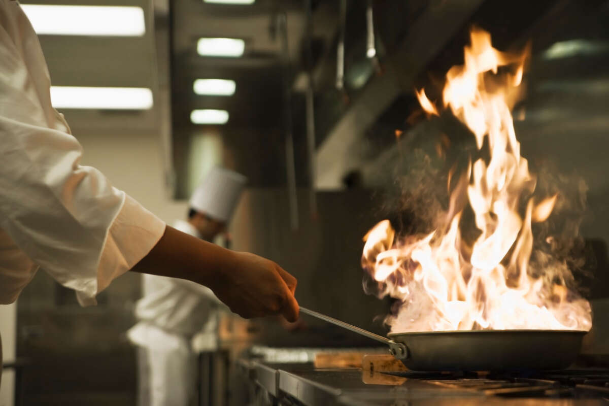Chef holds flaming pan in restaurant kitchen