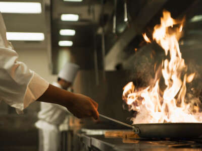 Chef holds flaming pan in restaurant kitchen