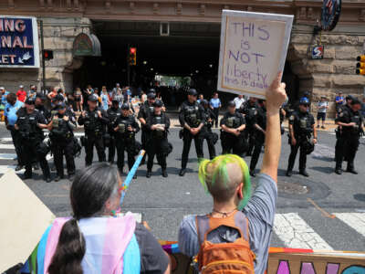 a protester holds up a sign reading "THIS IS NOT LIBERTY; THIS IS DEATH" while facing a line of cops