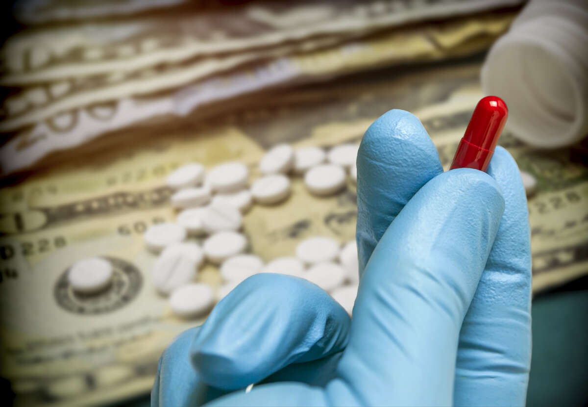 A gloved hand holds a pill capsule with money in the background