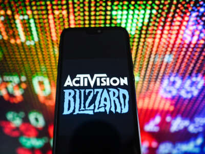 An Activision Blizzard logo is displayed on a smartphone with stock market percentages in the background.