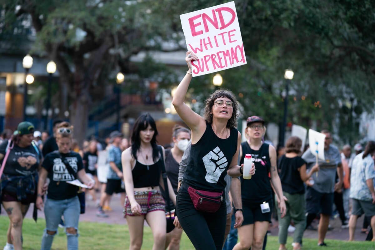 A protester holds a sign reading "END WHITE SUPREMACY" during an outdoor demonstration