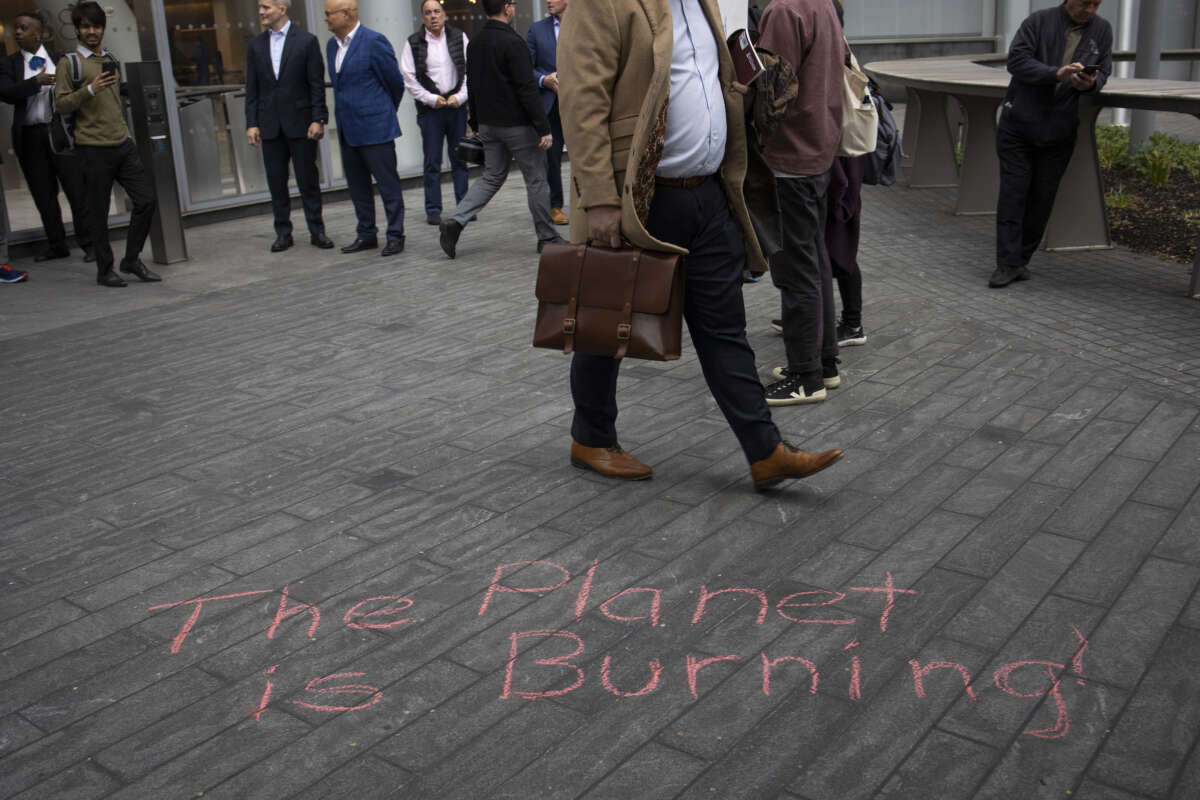 Bankers walk past chalk writing that says "The Planet is Burning!" as they leave work.