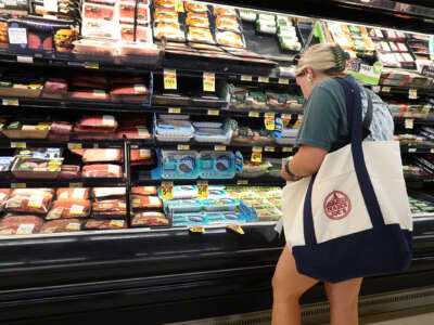 A blonde woman shops for groceries in the meat section of a grocery store.