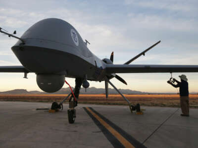 A predator drone sits on a runway against a dimly-lit sky