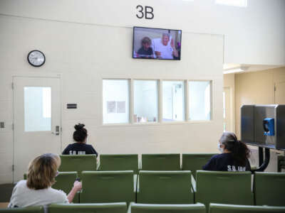 Women in a prison sit distanced from each other in a rec room while they watch a television program