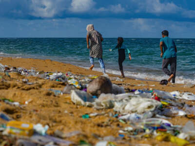A family walk down what would be a beautiful beach were it not completely littered with plastic garbage