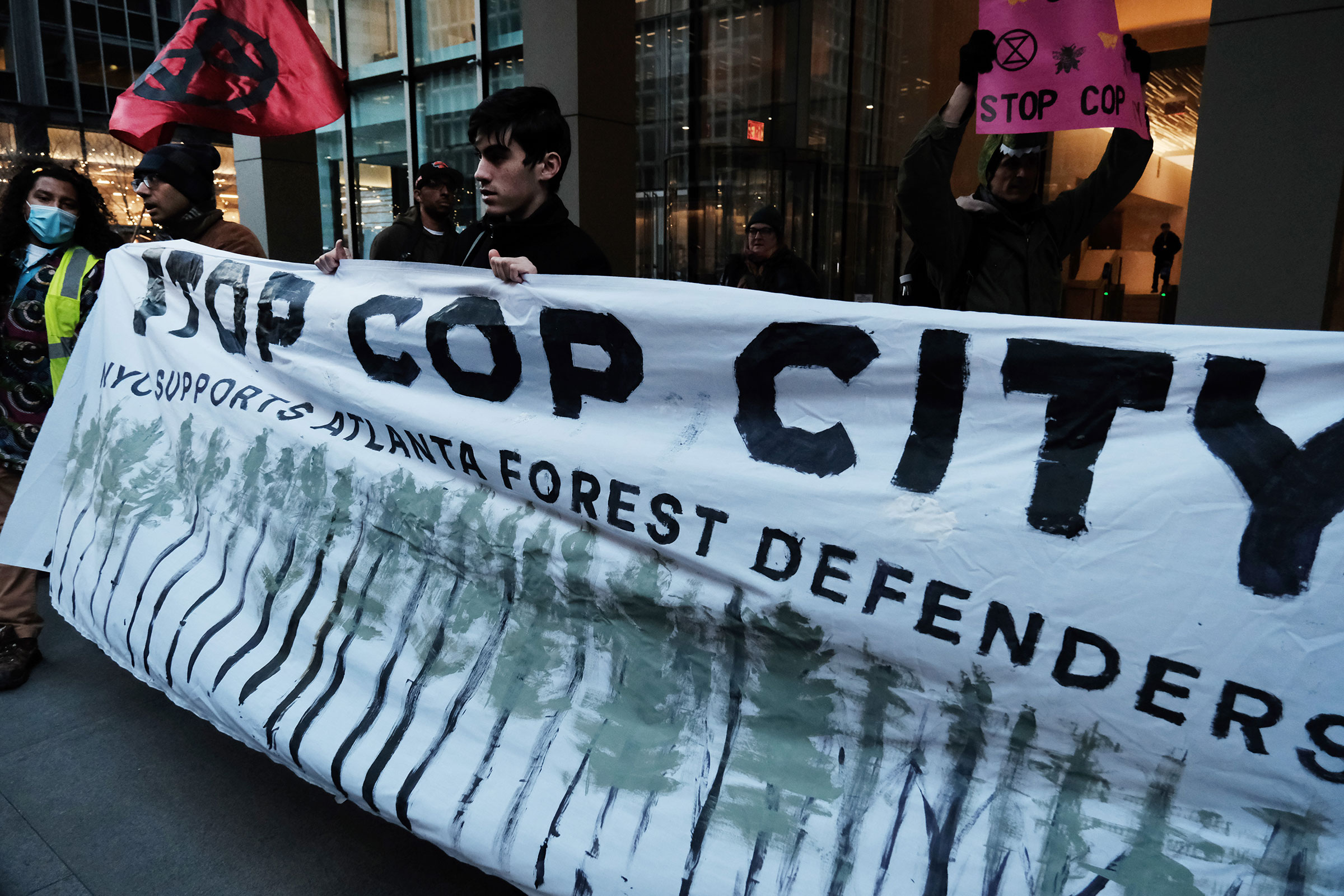 People stand behind a banner reading "STOP COP CITY; NYC SUPPORTS ATLANTA FOREST DEFENDERS" during an outdoor protest