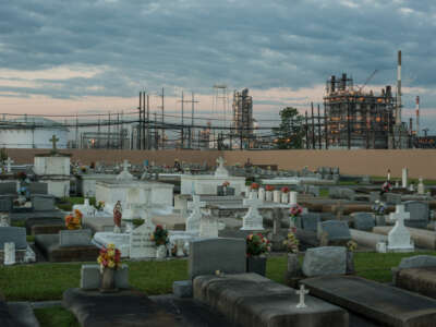 A petrochemical plant is seen on the horizon, looming over a graveyard in the foreground