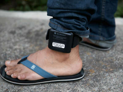 A foot is seen with an ankle monitor shackled to its ankle