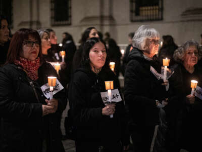 Women hold candles and small placards reading "NUNCA+" during an outdoor vigil