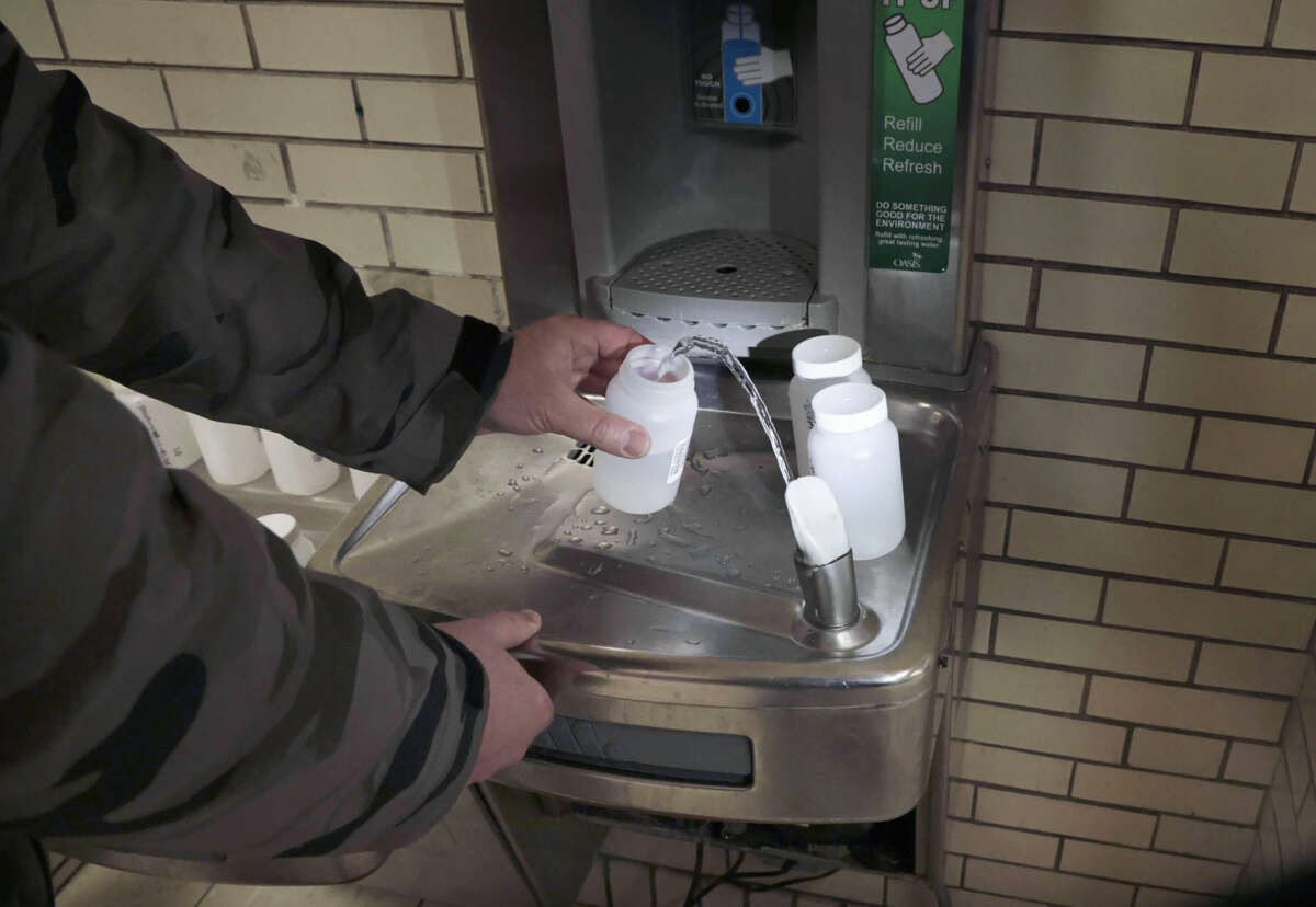 A person collects water from a drinking fountain in small specimen containers