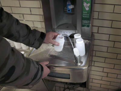 A person collects water from a drinking fountain in small specimen containers