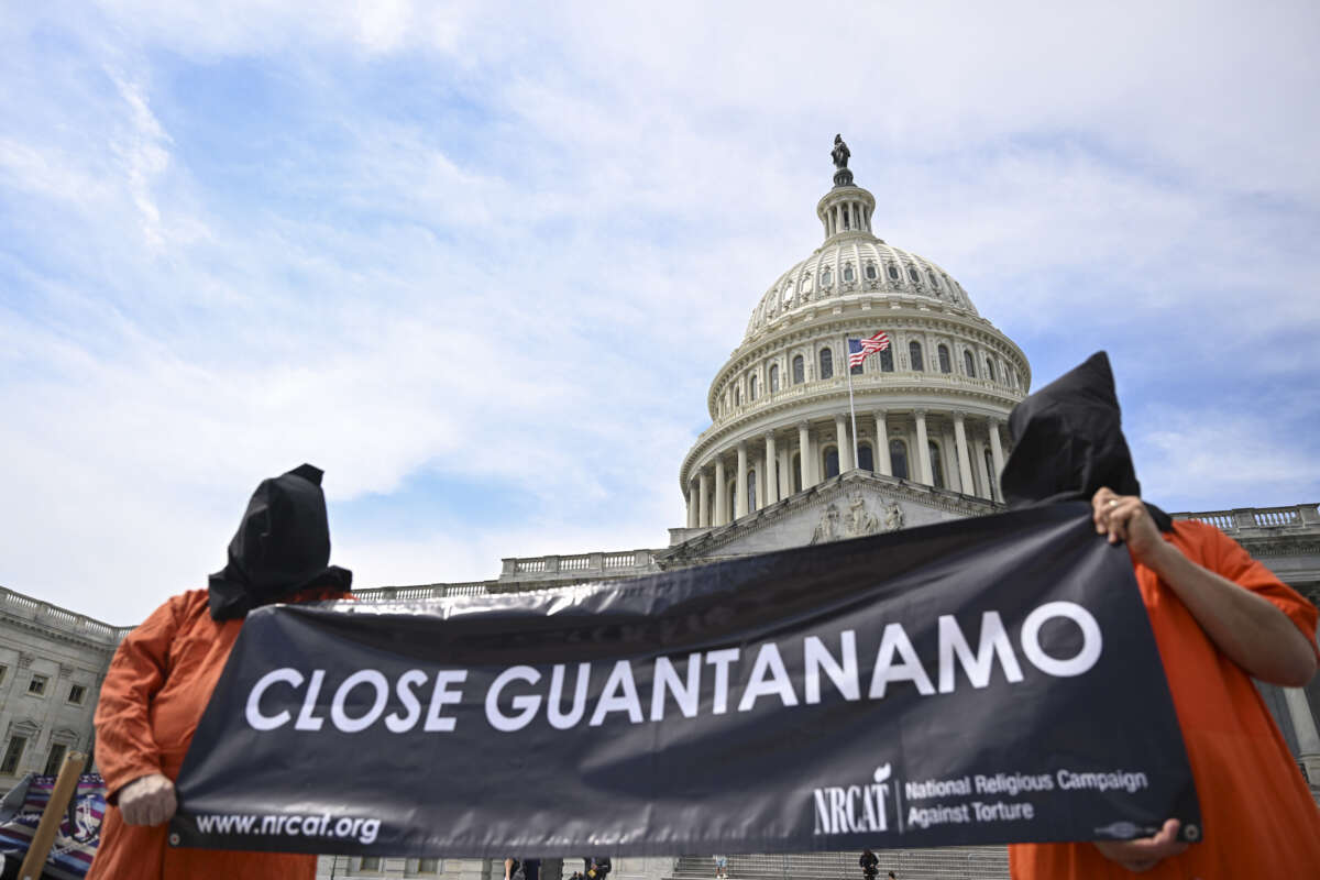 Two demonstrators in orange jumpsuits wearing black hoods carry a sign saying "Close Guantanamo" in front of the Capitol.