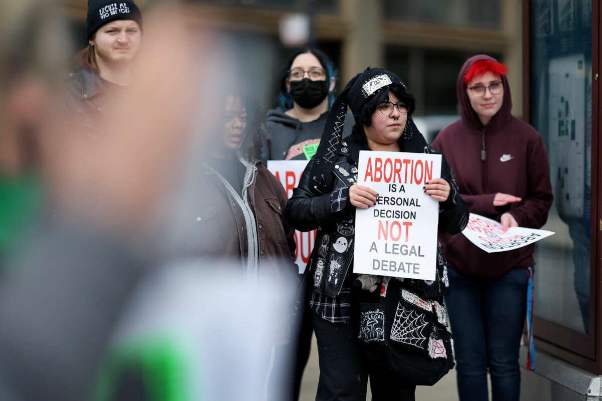 A protester in an adorable goth outfit holds a sign reading "ABORTION IS A PERSONAL DECISION NOT A LEGAL DEBATE" during an outdoor rally