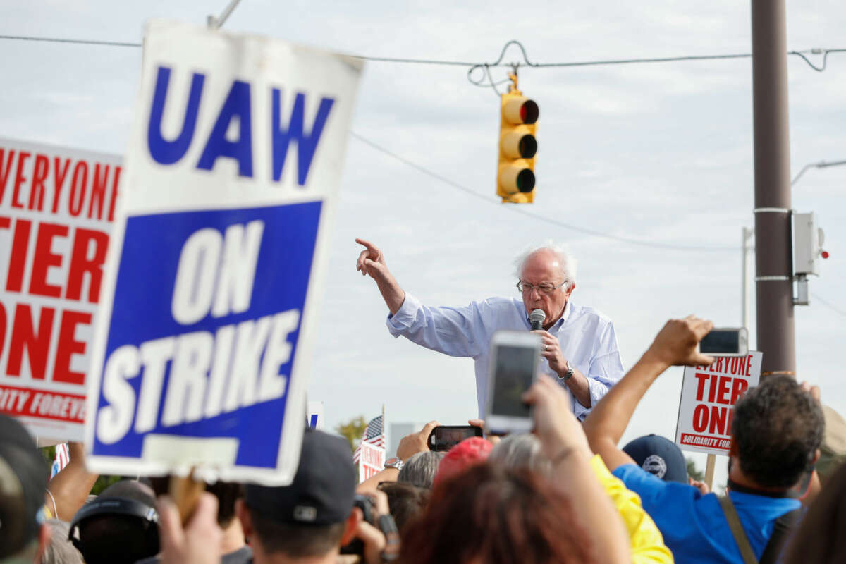 Bernie Sanders speaks passionately to rallying United Auto Worker members, one of whom are holding signs reading "UAW ON STRIKE"