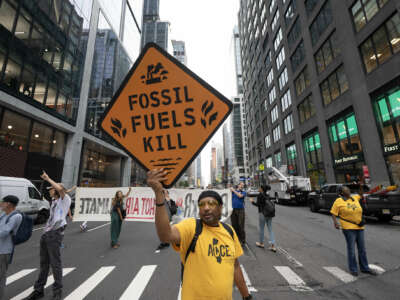 A protester holds a fake road sign reading "FOSSIL FUEL KILLS" during an outdoor street protest