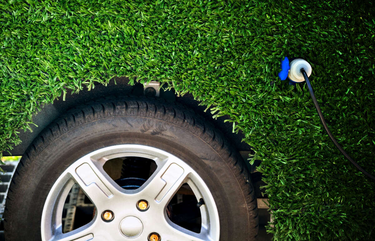 Electric car with astroturf greenery cover over all but the tire is charging via plug