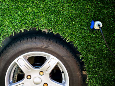 Electric car with astroturf greenery cover over all but the tire is charging via plug