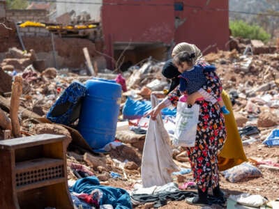 Two women and a child look for items in the rubble of their home in the village of Imzalin in Morocco